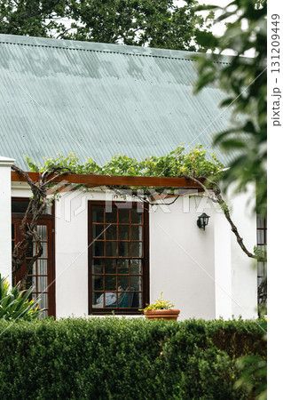 portion of a residential building classic architectural style. white facade, green roof. Large windows with wooden frames. building surrounded by lush vegetation 131209449