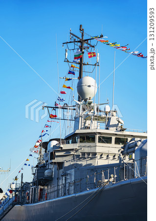 Close-up of naval warship mast decorated with colorful maritime signal flags on clear sky. Concept of navy tradition, marine communication, military ship ceremony 131209593