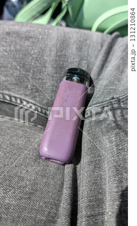 A stylish purple vaping device rests on trendy denim jeans, showcasing its modern aesthetic A stylish purple vaping device rests on trendy denim jeans, showcasing its modern aesthetic 131210864