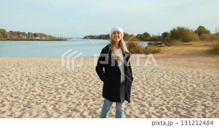 Happy young woman standing on sunny beach looking away, wear jacket, sea coast background Happy young woman standing on sunny beach looking away, wear jacket, sea coast background 131212484