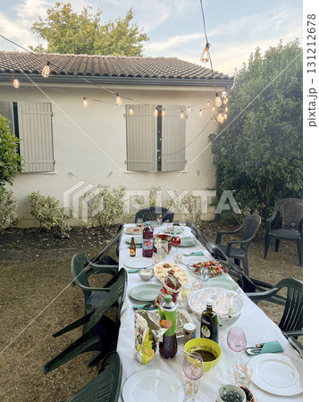 Gathering around a large family table in a backyard during evening time 131212678