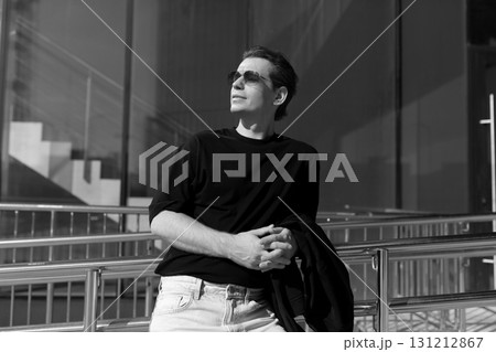 Man in sunglasses stands confidently outside a modern building on a sunny day with a relaxed pose Man in sunglasses stands confidently outside a modern building on a sunny day with a relaxed pose 131212867