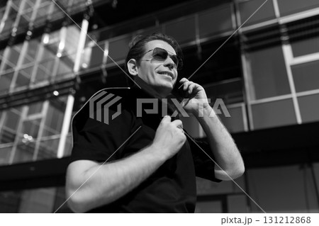 Man in sunglasses making a phone call outside modern building on a sunny day Man in sunglasses making a phone call outside modern building on a sunny day 131212868