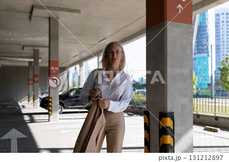 Woman dressed in business attire stands in urban parking lot during daytime while checking her phone Woman dressed in business attire stands in urban parking lot during daytime while checking her phone 131212897