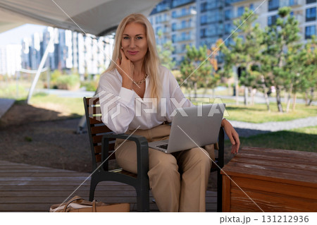 Professional woman working on laptop outside in modern urban park setting during sunny day 131212936