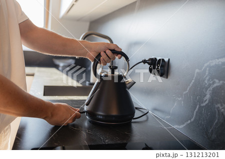 Man placing black electric kettle on modern kitchen stove Man placing black electric kettle on modern kitchen stove 131213201