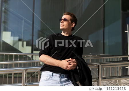 Stylish young man in sunglasses enjoying a sunny day outside a modern building in an urban setting 131213428