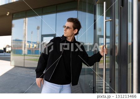 Man in sunglasses opens glass door outside modern building on sunny day 131213466