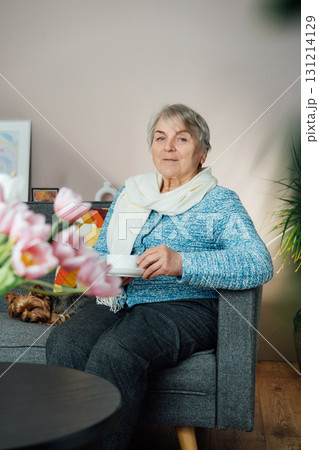 Smiling mature woman with dog pet relaxing at home with cup of tea, positive senior sitting on couch in modern living room looking satisfied feels good, older generation happy retired time enjoy life 131214129