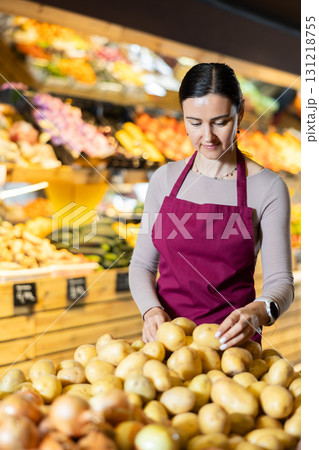 Middle-aged female seller putting potatoes on counter in grocery market 131218755