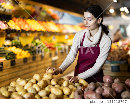 Young woman seller puts potatoes in vegetable shop Young woman seller puts potatoes in vegetable shop 131218767
