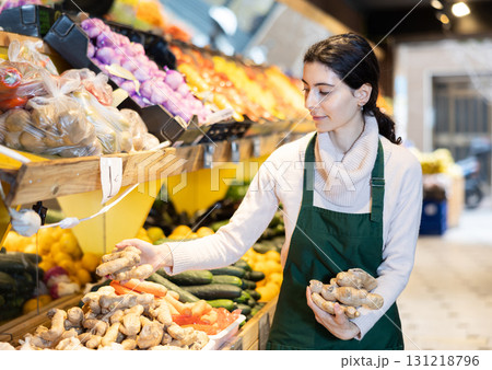 Young woman seller puts ginger in vegetable shop Young woman seller puts ginger in vegetable shop 131218796