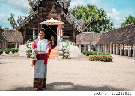 A woman in traditional Thai clothing stands with an umbrella in front of an ancient temple, showcasing cultural heritage. A woman in traditional Thai clothing stands with an umbrella in front of an ancient temple, showcasing cultural heritage. 131218810