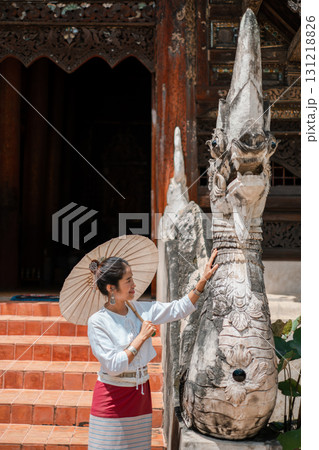 A woman in traditional attire with a parasol admires a detailed stone sculpture at an ancient temple. A woman in traditional attire with a parasol admires a detailed stone sculpture at an ancient temple. 131218826