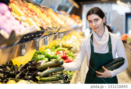 Young woman seller puts zucchini in vegetable shop 131218843