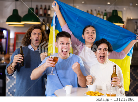 Happy friends of different ages drinking beer and celebrating the victory of the Ukrainian team in night bar Happy friends of different ages drinking beer and celebrating the victory of the Ukrainian team in night bar 131218866