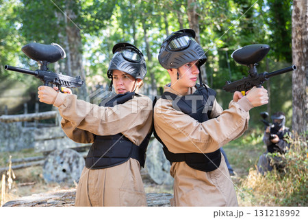 Boy and girl paintball players standing back-to-back and shooting Boy and girl paintball players standing back-to-back and shooting 131218992
