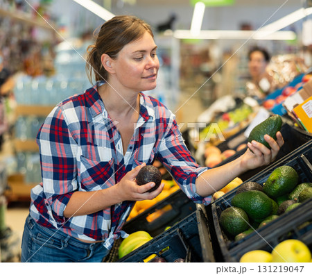Young female shopper choosing avocado in grocery store Young female shopper choosing avocado in grocery store 131219047