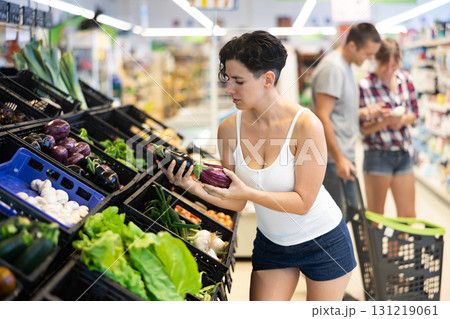 Portrait of cheerful female buyer taking fresh eggplant on supermarket 131219061