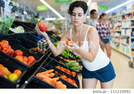 Interested young Hispanic woman choosing tomatoes in supermarket Interested young Hispanic woman choosing tomatoes in supermarket 131219092