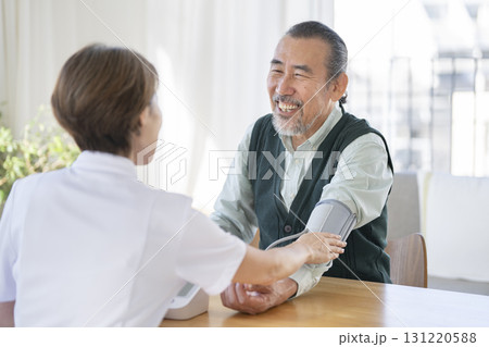 医療スタッフに血圧測定をしてもらう笑顔の70代の男性 131220588