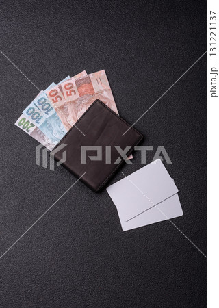 The white plastic card as a symbol of cashless payments on the background of cash paper money of Brazil 131221137