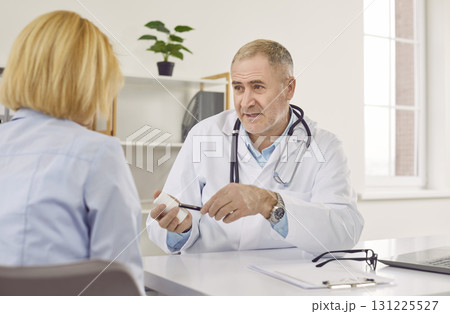 Mature male doctor sitting at his office and consulting female patient Mature male doctor sitting at his office and consulting female patient 131225527