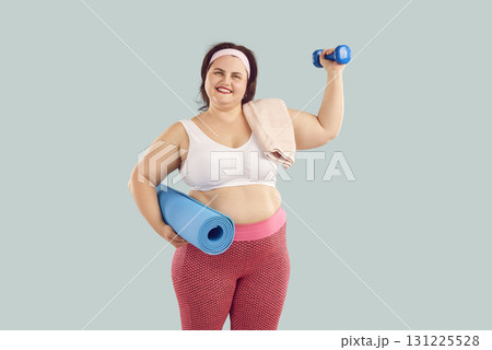 Portrait of happy chubby overweight young woman with dumbbell and fitness mat 131225528