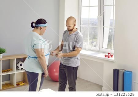 Young male nurse measure waist for a fat plump overweight young woman after doing sport exercises. Young male nurse measure waist for a fat plump overweight young woman after doing sport exercises. 131225529