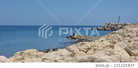 Peaceful Rocky Coastline with Fishermen and Breakwater 131225937