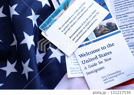 Permanent resident green card in envelope and guide for new immigrants lies on US flag Permanent resident green card in envelope and guide for new immigrants lies on US flag 131227530