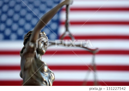 The statue of justice Themis or Justitia, the blindfolded goddess of justice against a flag of the United States of America The statue of justice Themis or Justitia, the blindfolded goddess of justice against a flag of the United States of America 131227542