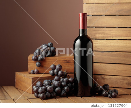 Bottle of red wine and blue grapes on a wooden background. 131227904