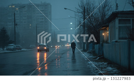 Seasonal depression. Solitary figure walks down dimly lit, wet street on foggy evening, with cars passing by and warm light glowing from nearby house 131227983