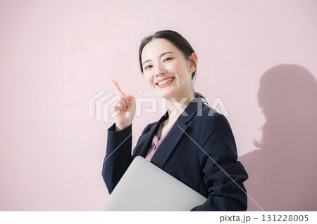 パソコン持ってスーツを着た立つ若いかわいい女性のビジネス上半身　かわいいピンク背景の営業など 131228005