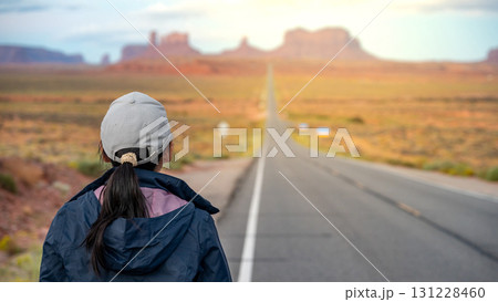 Female tourist standing off the highway looking at the long road view leading to Monument Valley Female tourist standing off the highway looking at the long road view leading to Monument Valley 131228460