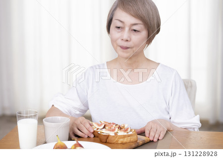 朝食のパンを食べるシニア女性   131228928