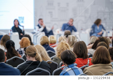 Diverse audience attends panel discussion at conference with speakers on stage and engaged attendees 131229438