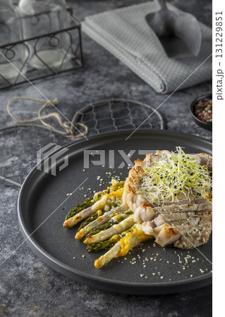 Sliced pork tenderloin with grilled asparagus and cheese sauce, garnished with microgreens 131229851