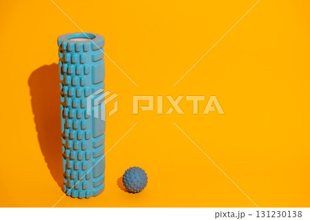 Vertical foam roller with spiky massage ball on bright yellow minimalist wellness gear copy space Vertical foam roller with spiky massage ball on bright yellow minimalist wellness gear copy space 131230138