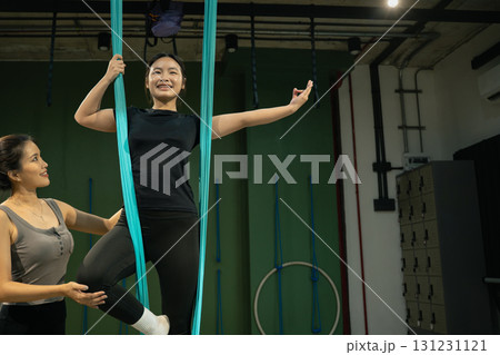 Yoga instructor assisting woman practicing aerial yoga with hammock support in fitness studio 131231121