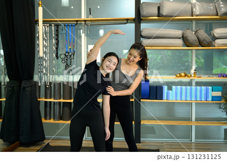 Female trainer assisting young woman with side stretching exercise in a modern yoga studio 131231125
