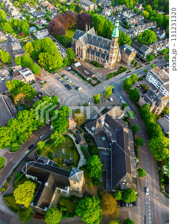 Aerial view of a European town with a tall green spire gothic church at its center, surrounded by red roofed houses, winding streets, trees, and fields blending into rural outskirts. Aerial view of a European town with a tall green spire gothic church at its center, surrounded by red roofed houses, winding streets, trees, and fields blending into rural outskirts. 131231320