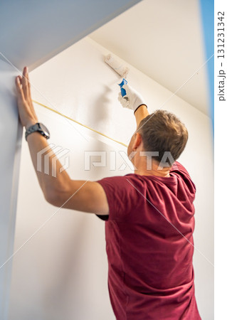 Man painting the wall with a roller in white during home renovation. Interior improvement, surface transformation and DIY work with paint tools. Man painting the wall with a roller in white during home renovation. Interior improvement, surface transformation and DIY work with paint tools. 131231342