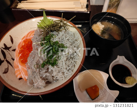 A Japanese meal set with a rice bowl topped with raw salmon, tiny fish, and salmon roe, served with miso soup and pickles. Fresh toppings and side dishes highlight a traditional dining experience in 131231821