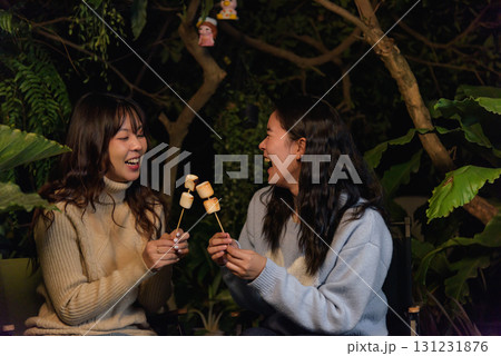 Winter camp outdoor, two happy women friends enjoying forest evening, roasting delicious marshmallow treats, creating warm winter memories together with delight. 131231876