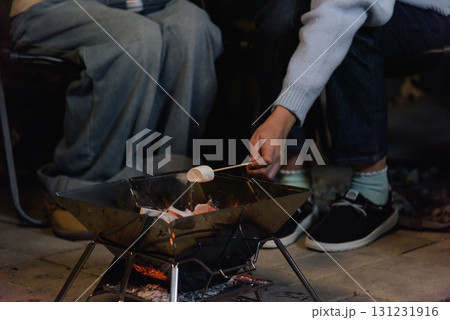 Winter camp outdoor, happy woman friend people enjoy forest fire, roasting marshmallow on stick, creating warm memories together during cozy winter evening adventure. 131231916