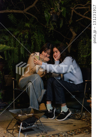 Winter camp outdoor, happy women friends enjoy forest night, people gather around fire pit, cozy warm sweaters create atmosphere during winter evening. 131231917