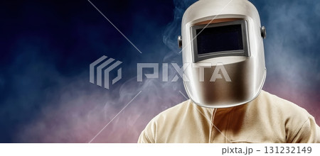 A welder, shrouded in smoke, stands protectively behind a silver welding mask 131232149