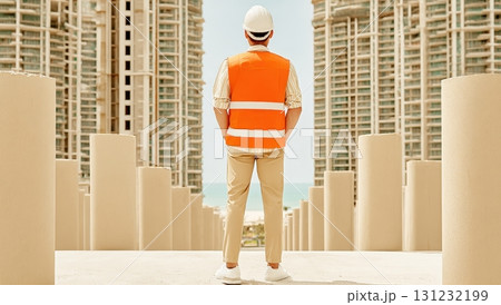 A construction worker in an orange safety vest stands on a rooftop, overseeing a city's skyline of modern highrises 131232199